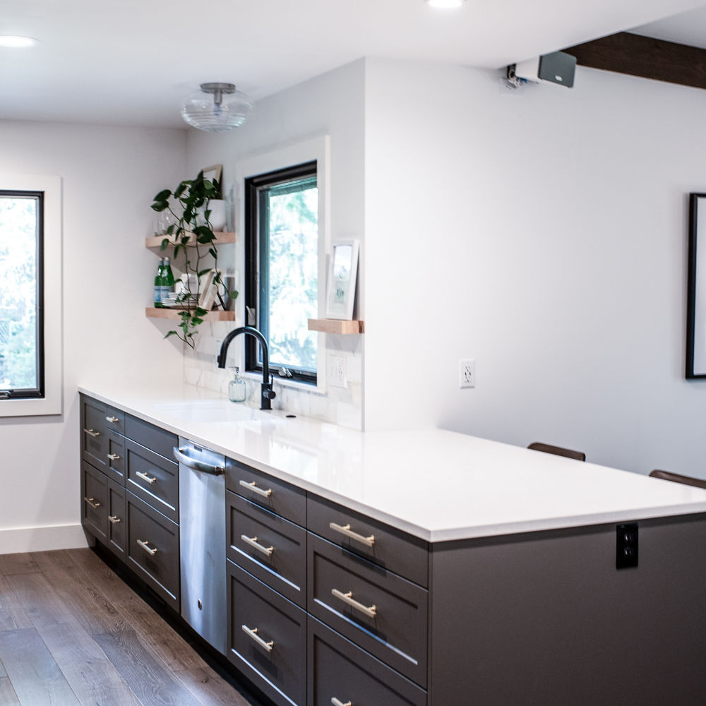 a simple kitchen with dark brown cabinets, white quartz countertops, and plenty of natural lighting.