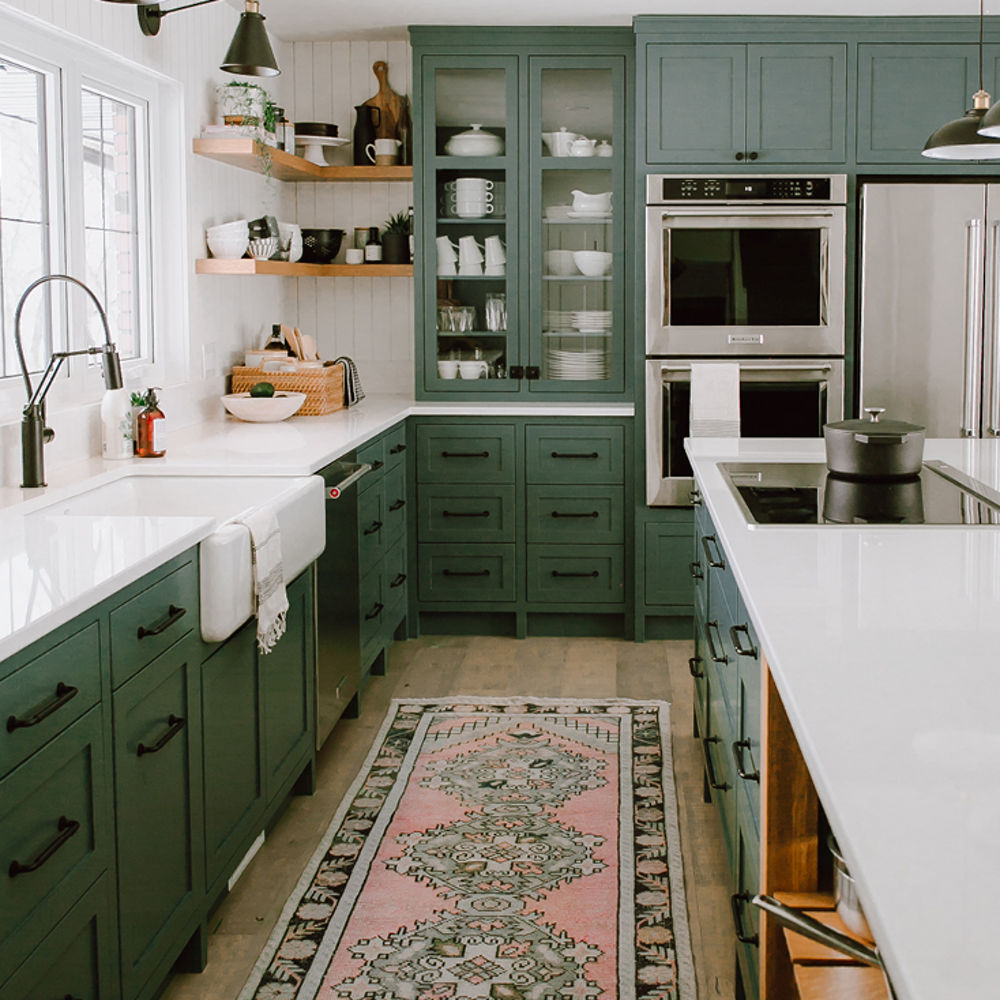 a farmhouse kitchen with green upper and lower cabinets, white quartz countertops, center island, farmhouse sink, and open wooden shelving