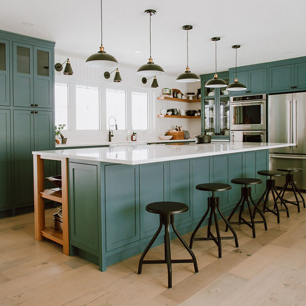 a traditional kitchen with green upper and lower cabinets, a green center island, wooden accents, light wooden floors, and white quartz countertops.