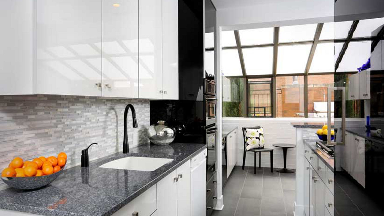 a modern galley kitchen with white cabinets, blue-ish gray quartz countertops, black appliances, and gray tiled floor