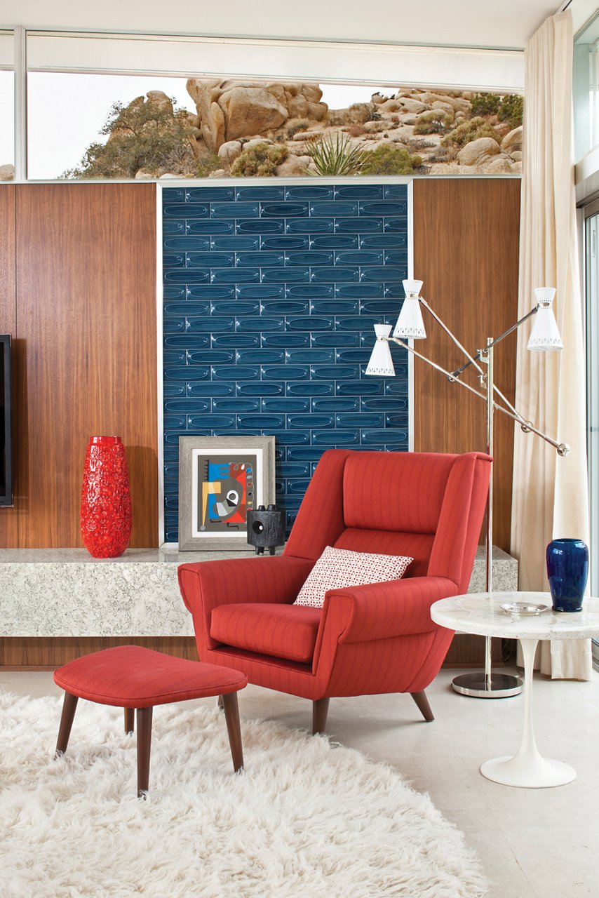 a mid-century modern living room with a red armchair and ottoman, a floating bench made from quartz, wooden paneling, and a fuzzy white rug.
