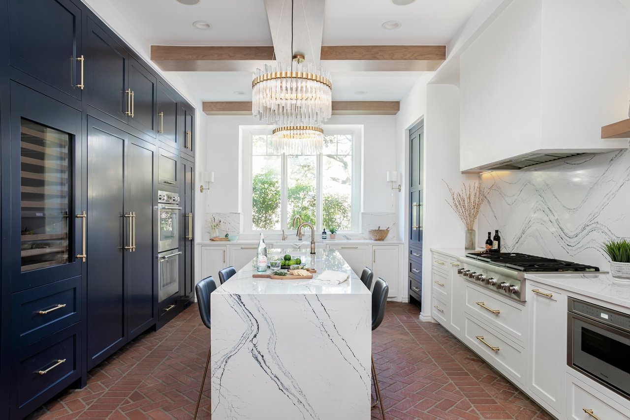 Cambria Portrush countertops and backsplash accenting a navy and white kitchen with gold chandelier lighting