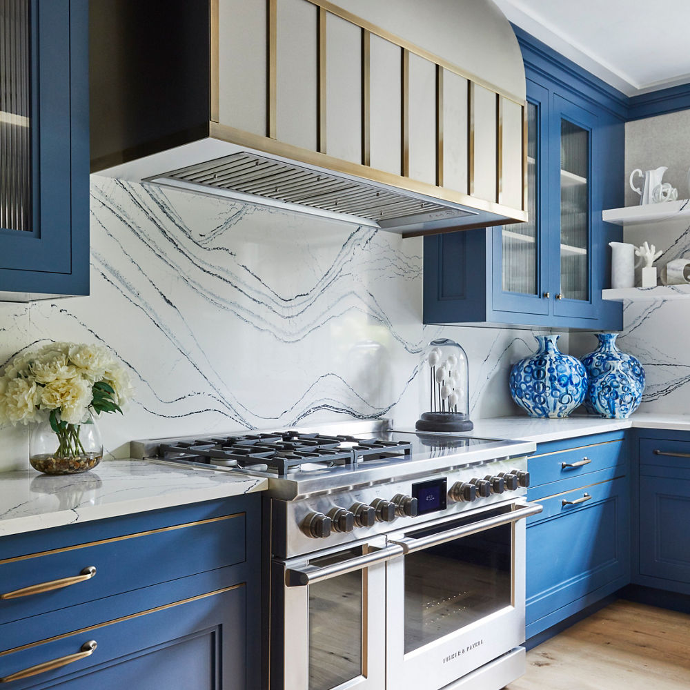 A kitchen with blue cabinets, gold hardware, and white and blue veined quartz backsplash and countertops.