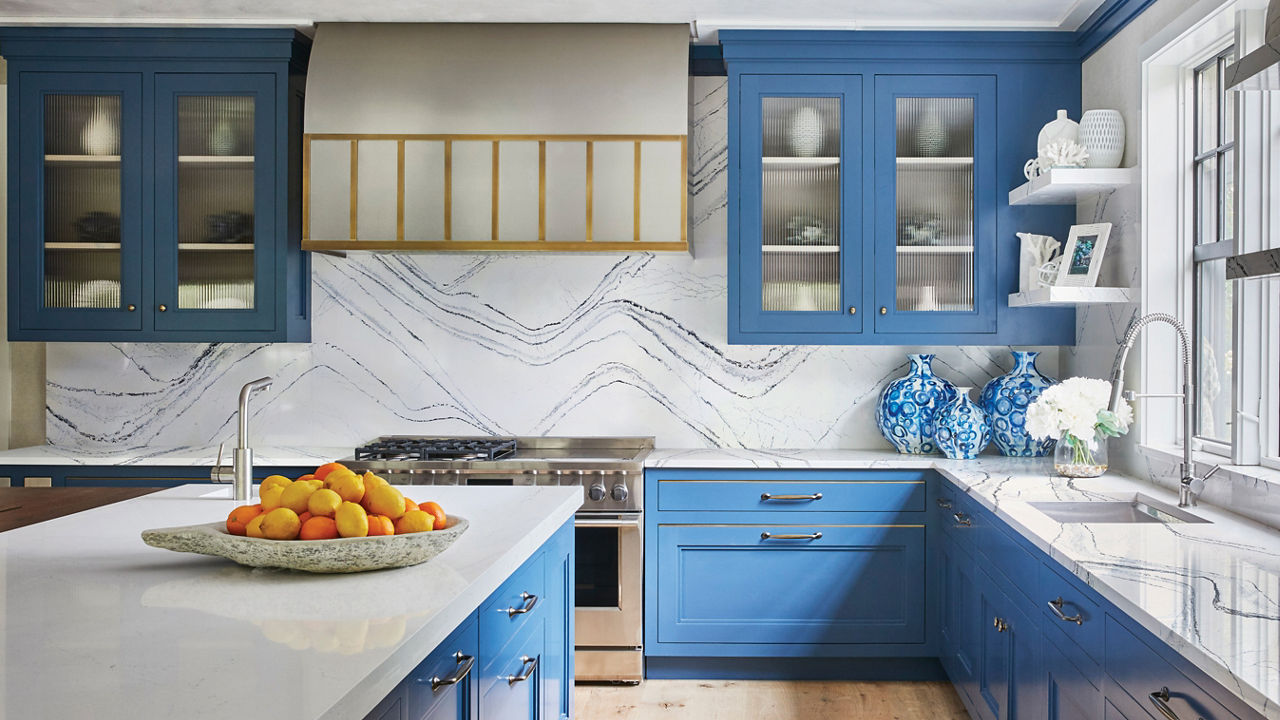 a luxurious blue and white kitchen with sky blue upper and lower cabinets, white quartz countertops with blue veining and matching quartz backsplash, with gold accents throughout. 