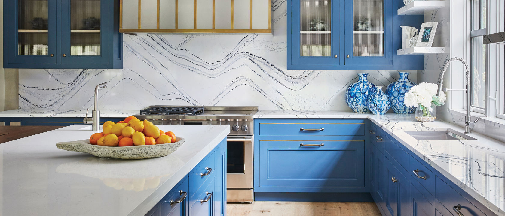 a luxurious blue and white kitchen with sky blue upper and lower cabinets, white quartz countertops with blue veining and matching quartz backsplash, with gold accents throughout. 