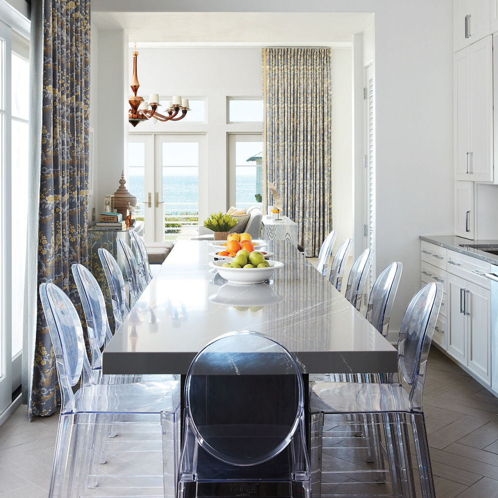 a stunning dining room with a table topped with gray quartz countertops and glass chairs.