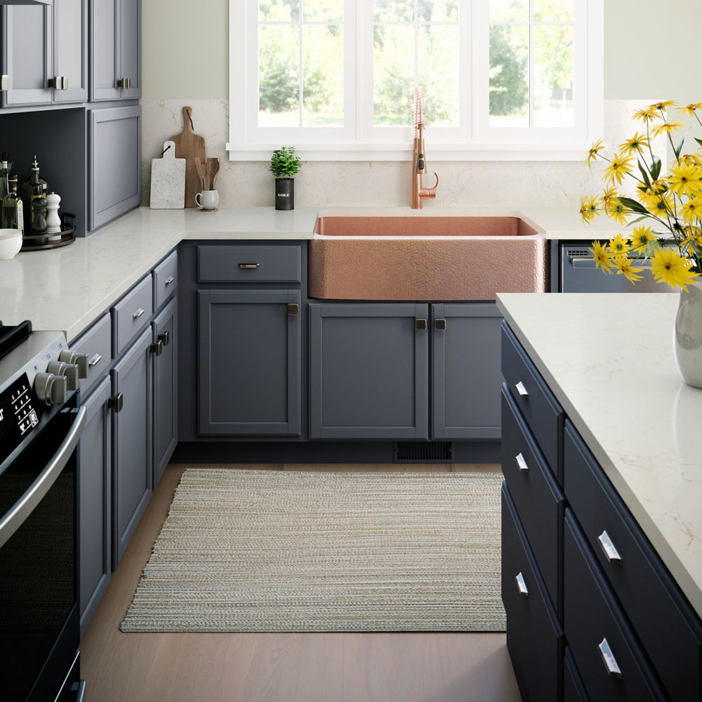 A welcoming kitchen with slate blue cabinets, warm white quartz countertops, a bold bronze farmhouse sink, and a large window.