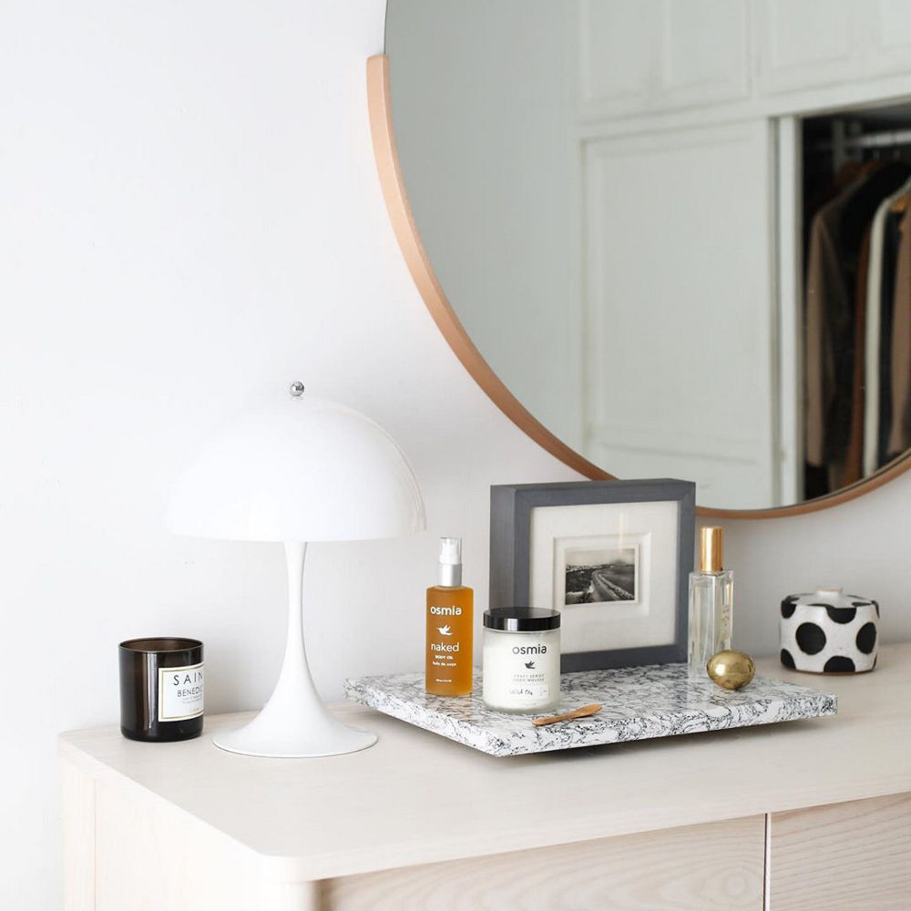 A bedroom vanity with a circular mirror and a small slab of quartz for perfume, candles, and pictures to sit on.