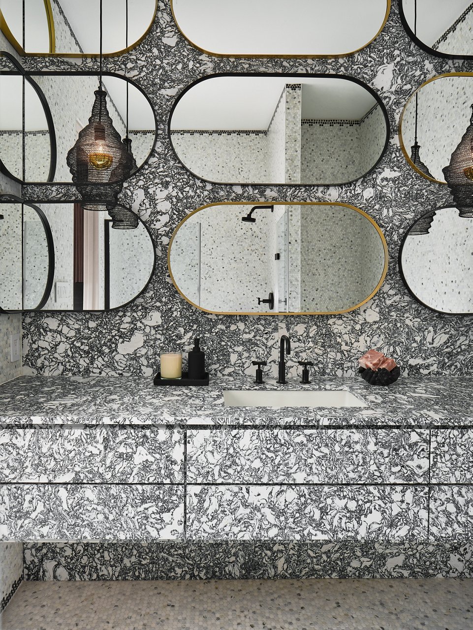 A bold bathroom with Rose Bay Matte Quartz countertops and matching backsplash, with multiple oval shaped mirrors in various neutral colors.