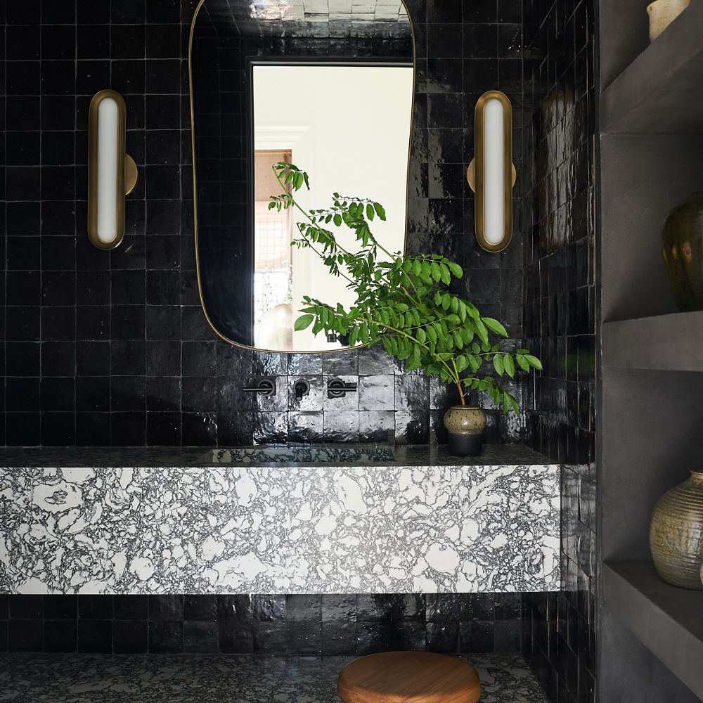 A bold floating bathroom vanity made from white and black quartz countertops with a sleek black tiled backsplash and gold and white mirror and sconces. 