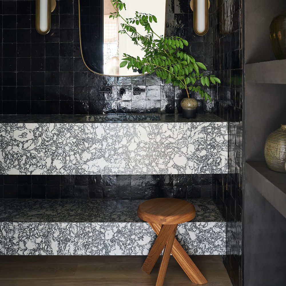 A bold floating bathroom vanity made from white and black quartz countertops with a sleek black tiled backsplash and gold and white mirror and sconces. 