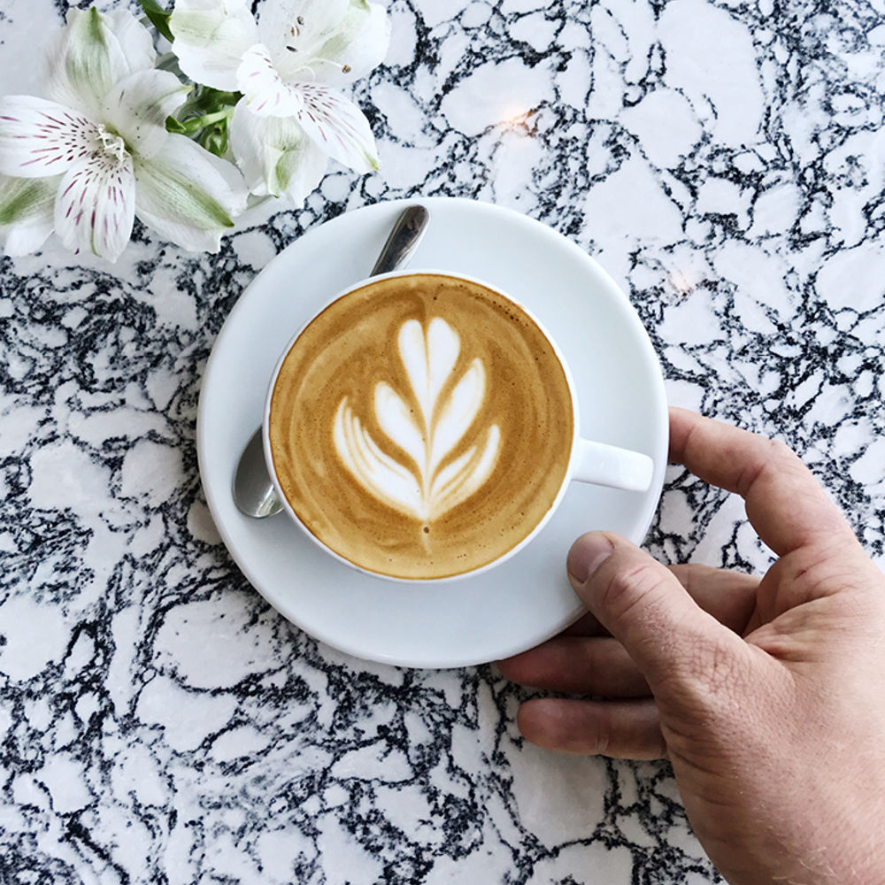 A coffee mug on a plate that is placed on a Cambria Rose Bay quartz countertop.