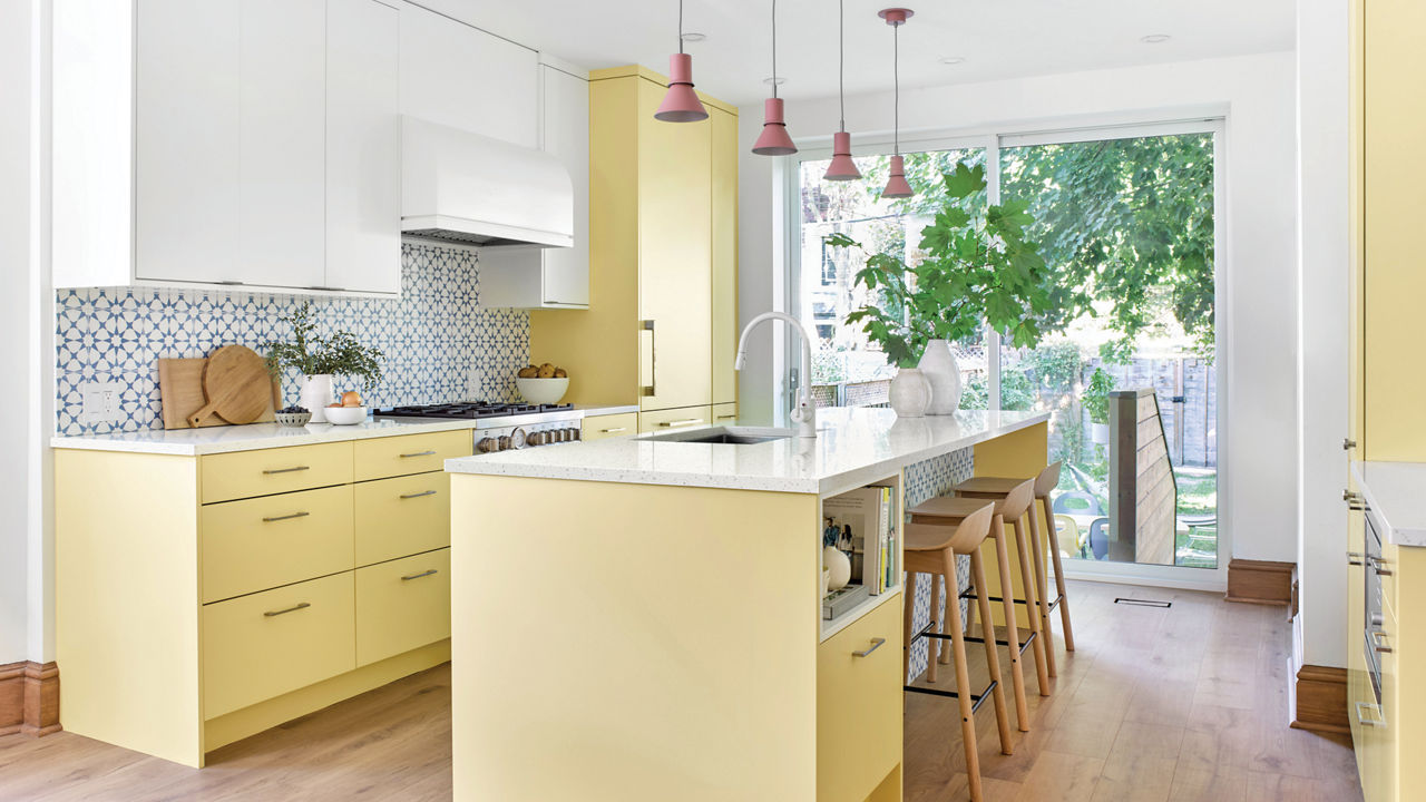 A bright kichen with yellow bottom and island cabinets, a large window, white upper cabinets and Cambria quartz Salt Lake countertops.