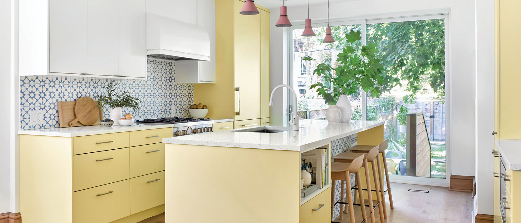 A bright kichen with yellow bottom and island cabinets, a large window, white upper cabinets and Cambria quartz Salt Lake countertops.