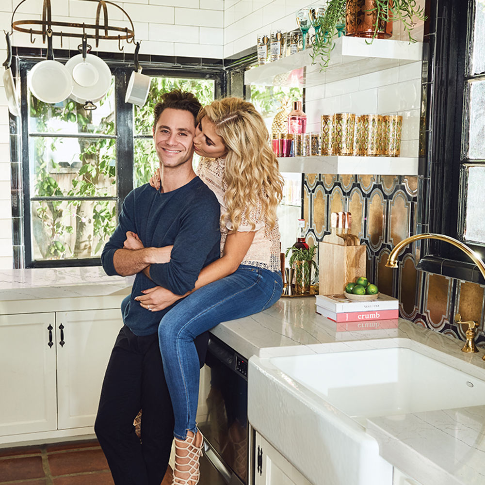 A woman sitting on top of her Cambria Ella Quartz kitchen countertop kissing her smiling husband.