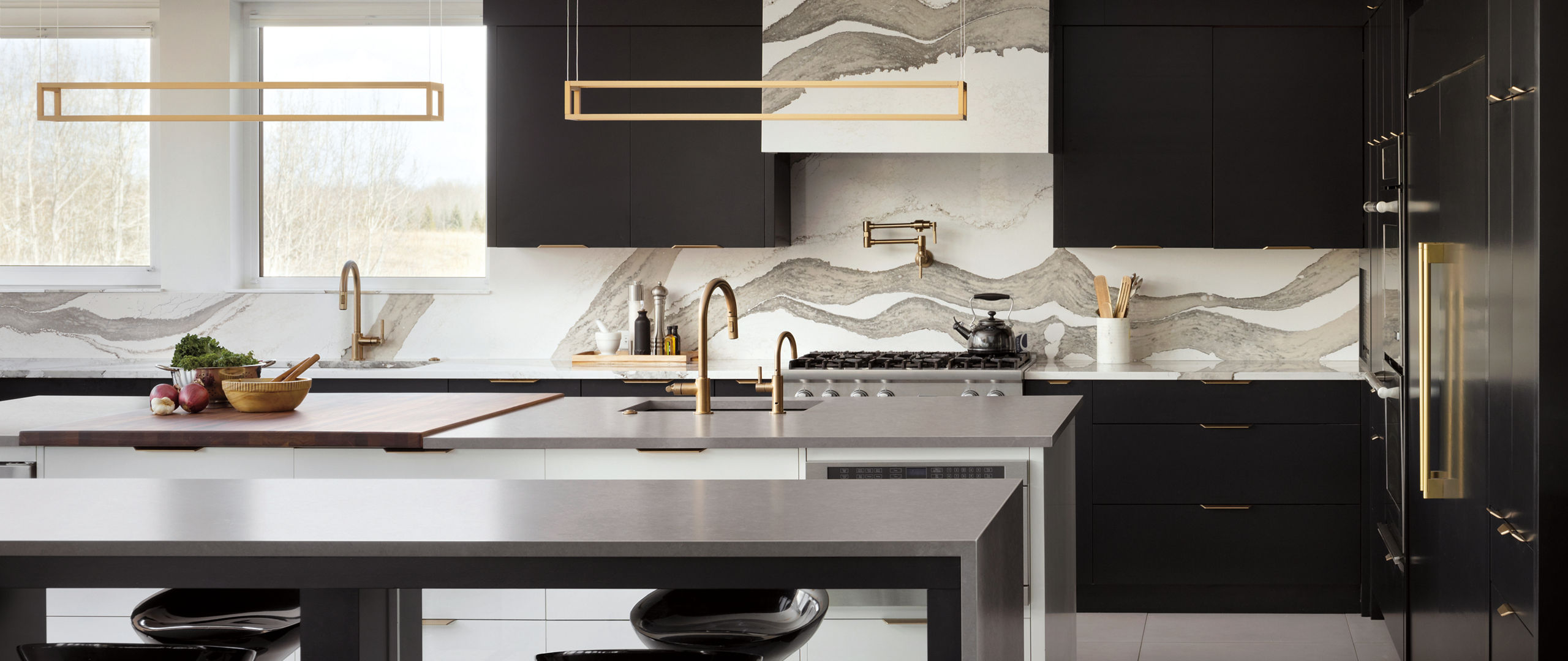 A luxurious kitchen with two islands topped with gray quartz, with black cabinets, and a white and gray veined quartz backsplash.