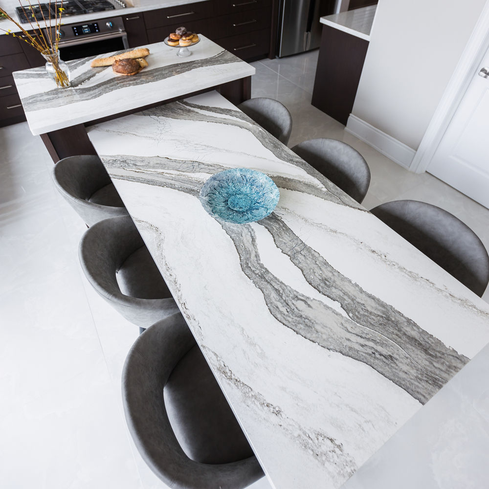 overhead view of a quartz table attached to an island topped with white and gray quartz countertop and 6 black chairs around.