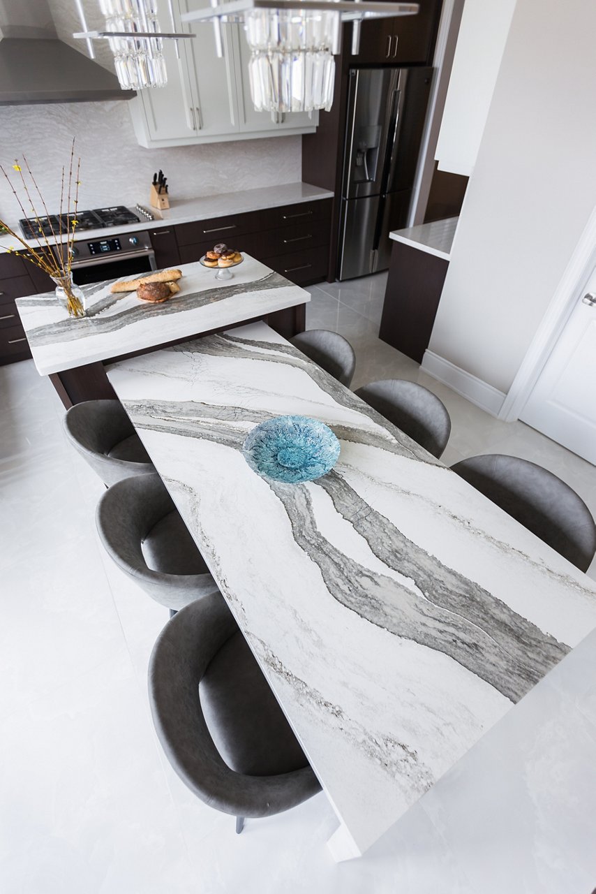 overhead view of a quartz table attached to an island topped with white and gray quartz countertop and 6 black chairs around.