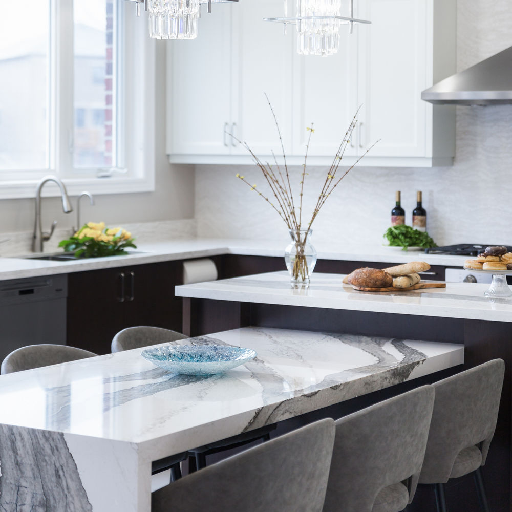a white and black kitchen with modern overhead lighting over a built in table from the island made from white and grey veined quartz countertops.