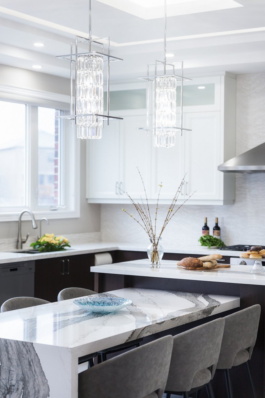 a white and black kitchen with modern overhead lighting over a built in table from the island made from white and grey veined quartz countertops.
