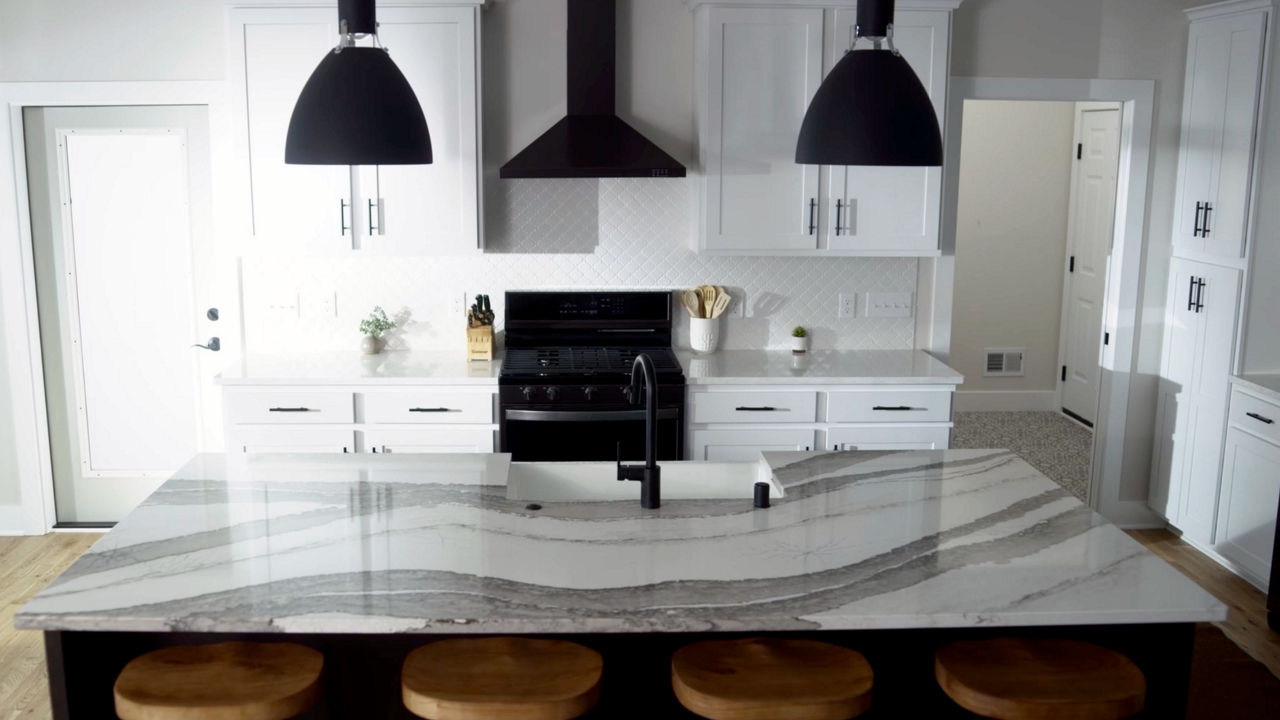 a traditional kitchen with white cabinets, black appliances, two black pendant lights over an island topped with white and gray veined quartz countertops.