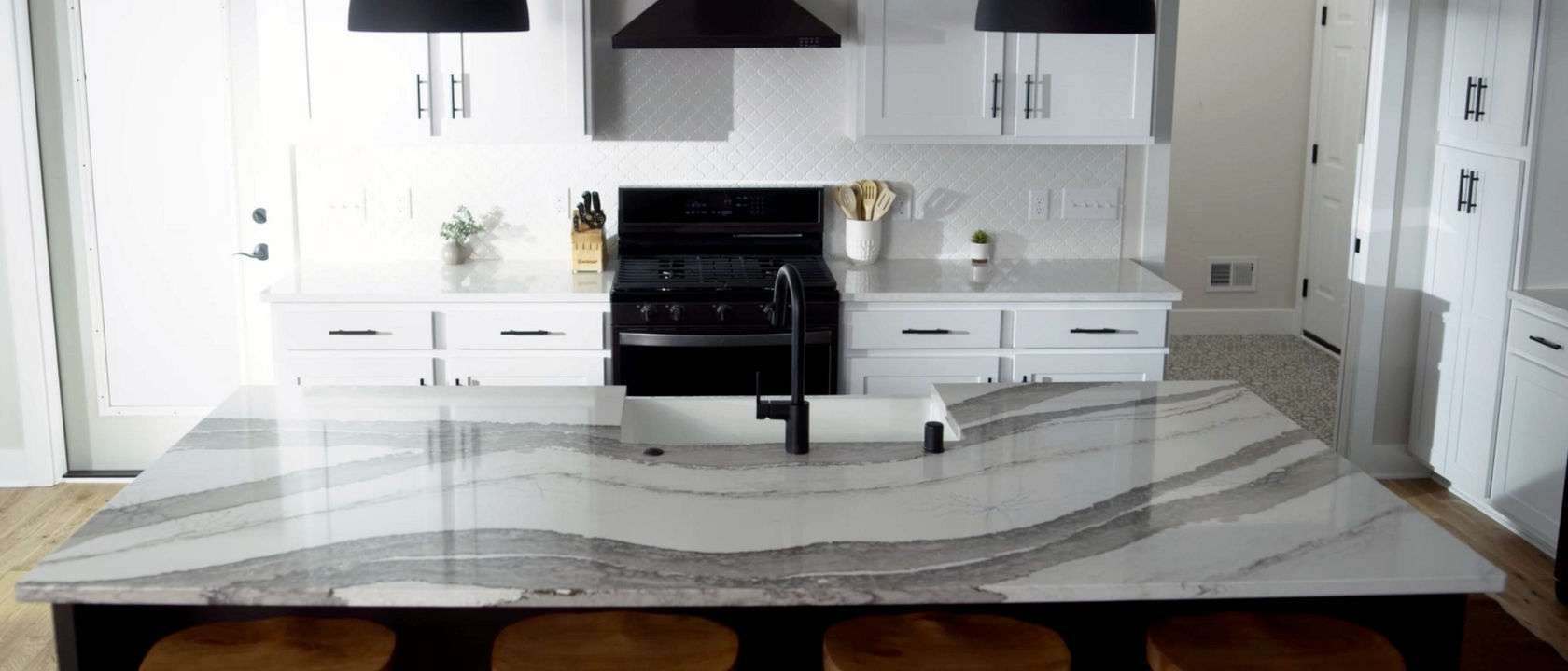 a traditional kitchen with white cabinets, black appliances, two black pendant lights over an island topped with white and gray veined quartz countertops.