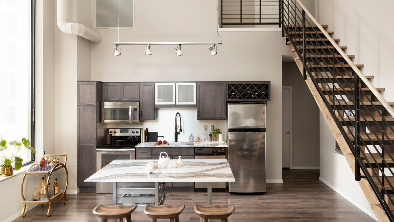 An open-concept loft kitchen with taupe gray cabinetry and Cambria Quartz Skara Brae countertops.