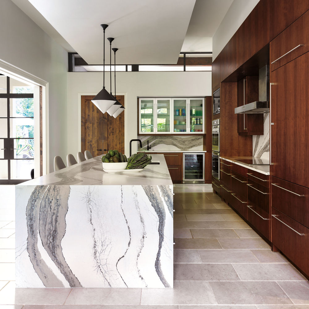 a modern kitchen with wooden cabinets, a double waterfall quartz island, tiled flooring, and a quartz backsplash.