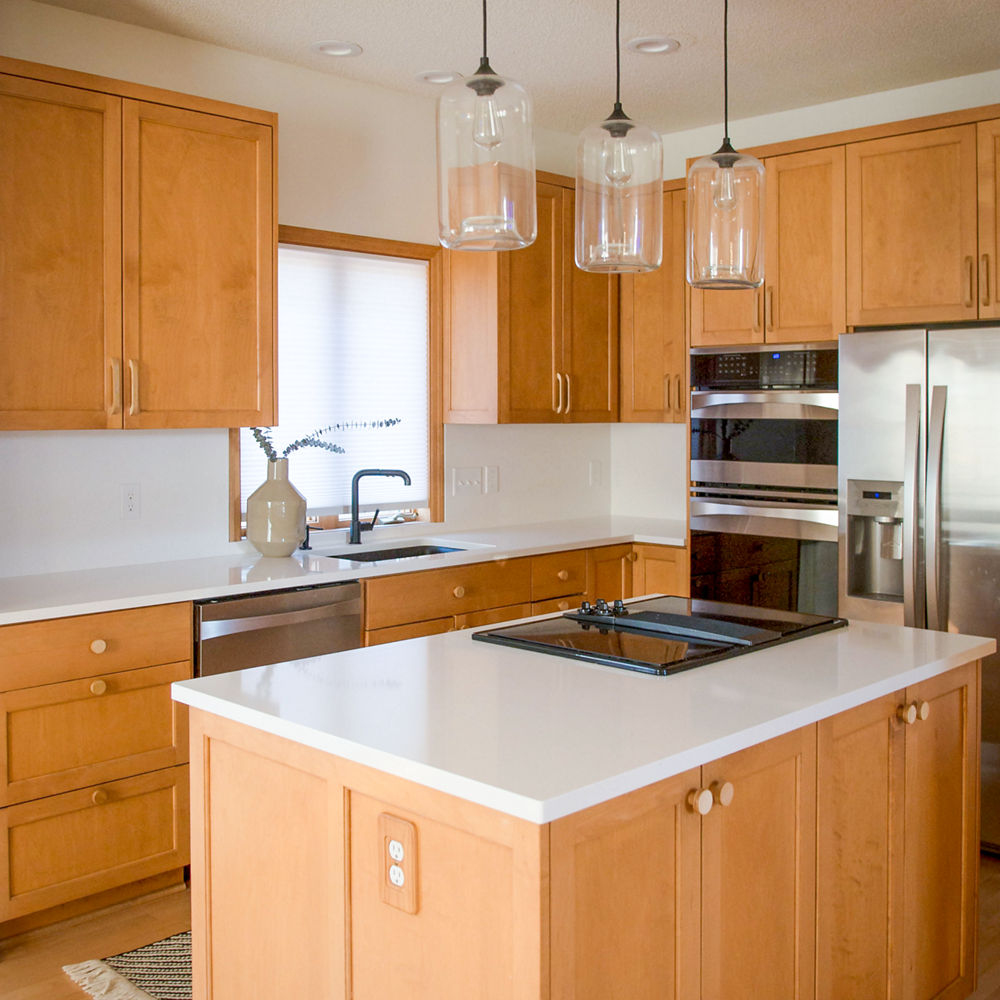 a warm kitchen with oak cabinets, Smithfield white quartz countertops, stainless steel appliances, and an island with a cooktop in it.