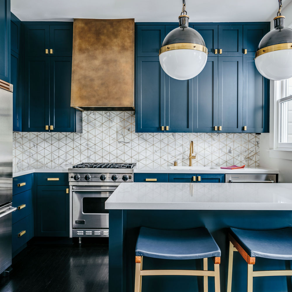 A luxurious blue kitchen with cobalt blue cabinets, gold hardware, white quartz countertops, and a unique tile backsplash.