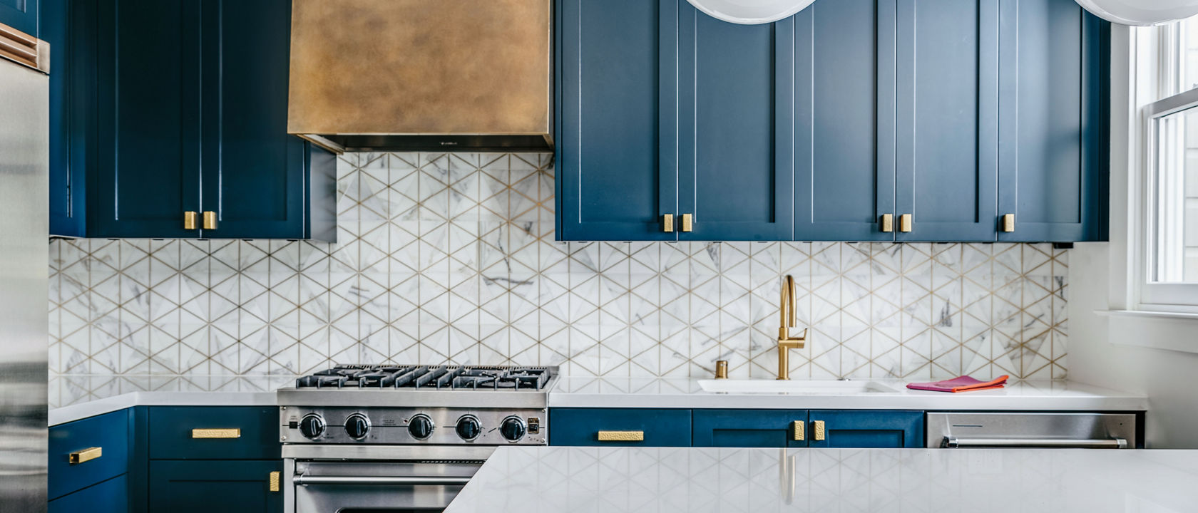 A luxurious blue kitchen with cobalt blue cabinets, gold hardware, white quartz countertops, and a unique tile backsplash.