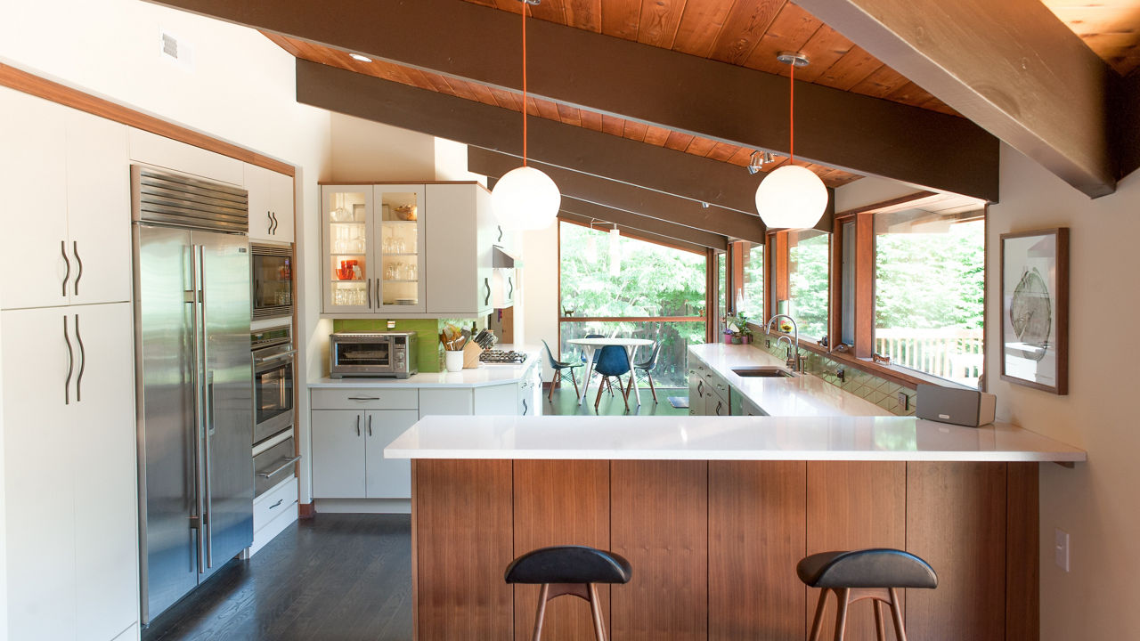 A warm kitchen with oak cabinets, half vaulted wooden ceilings, stainless steel appliances, and Snowdon White quartz countertops