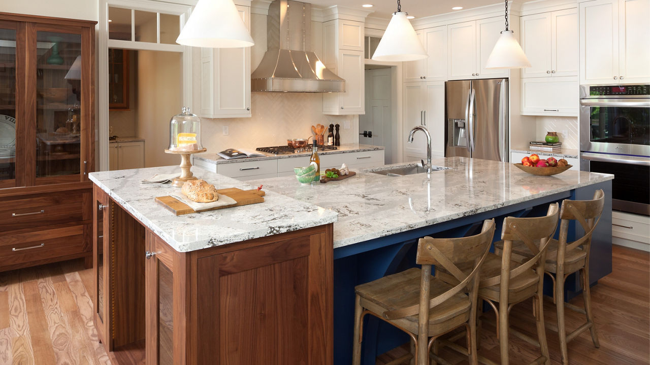 A kitchen island with brown cabinets, blue siding, and a Cambria Summerhill quartz countertop.