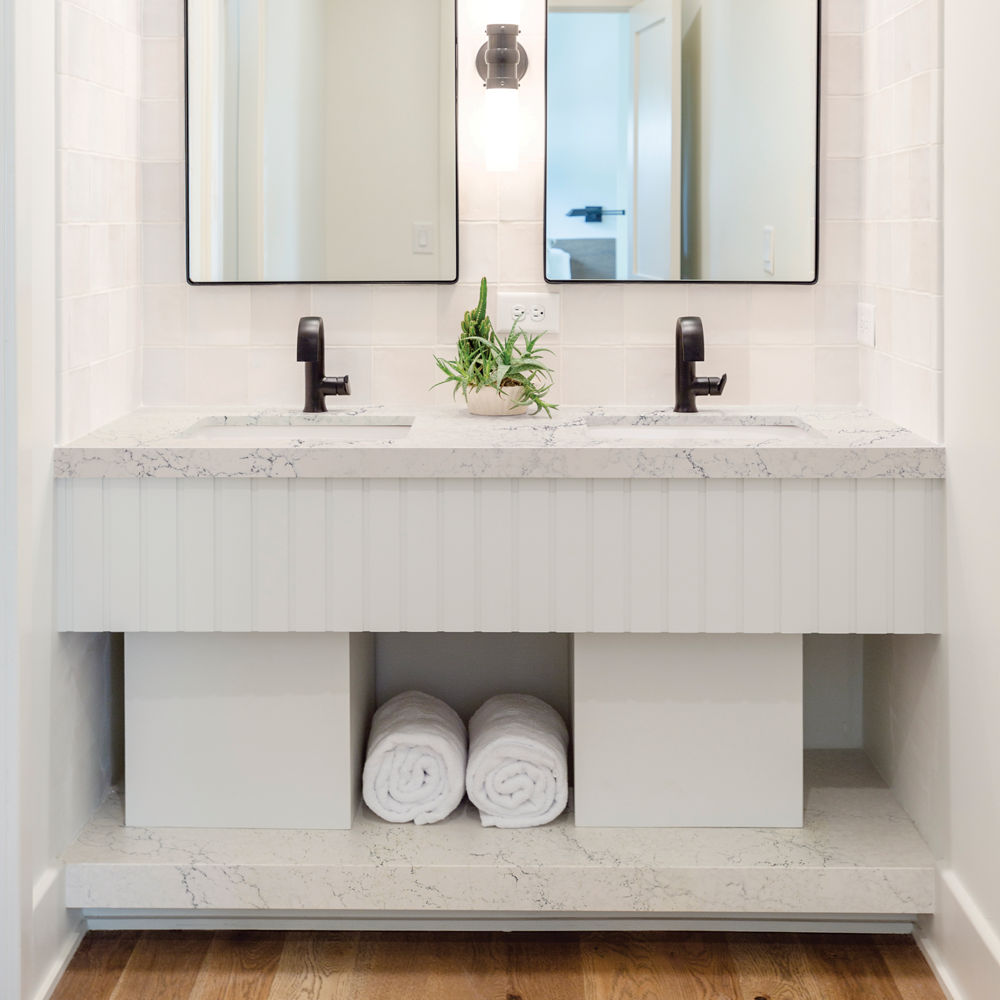 a bathroom with white vanity with white quartz countertops and based, two black mirrors, black hardware, and a spot for towels.