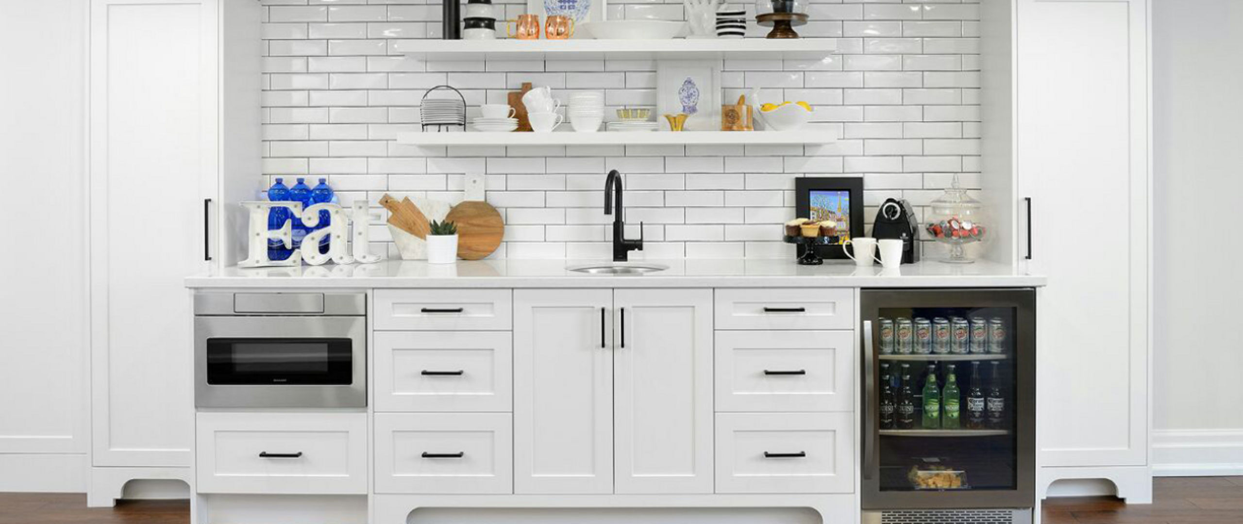 a wet bar with white cabinets, white quartz countertops, white subway tile, open shelving, and a mini fridge. 