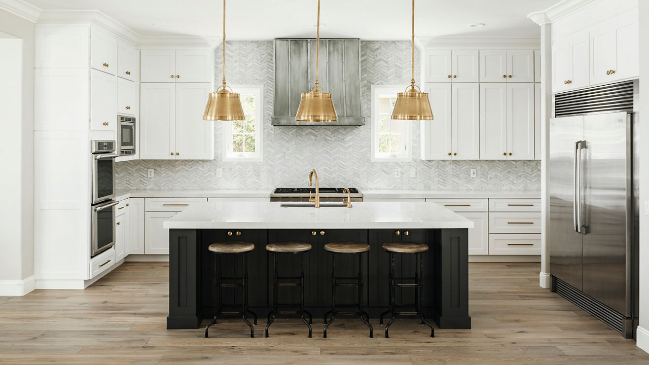 A white kitchen with a gray tile backsplash and gold light fixtures with Swanbridge quartz countertops