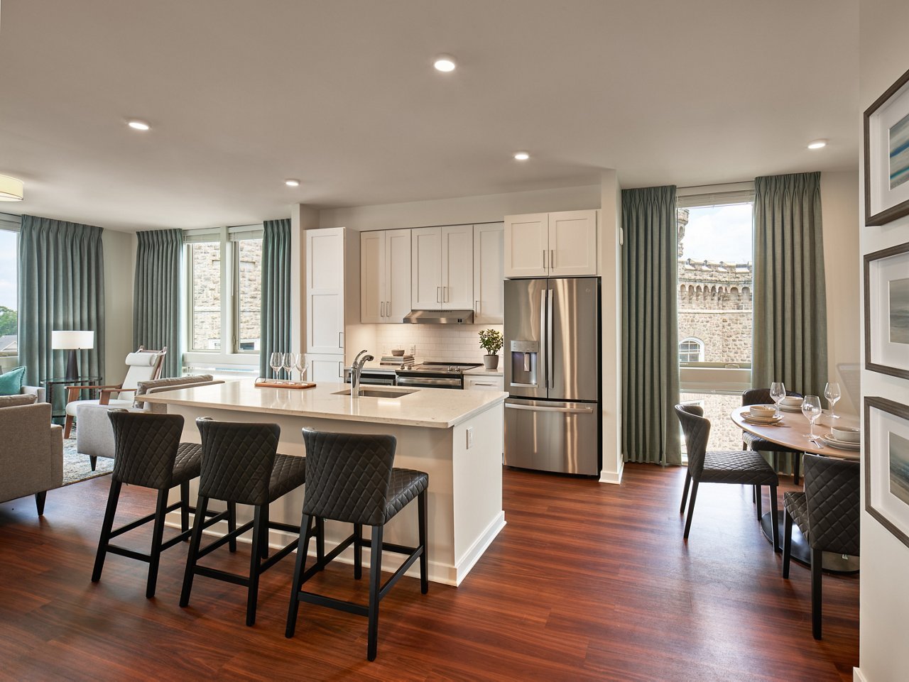 A traditional kitchen with white cabinets, white quartz countertops, black furniture, modern appliances, and green curtians.