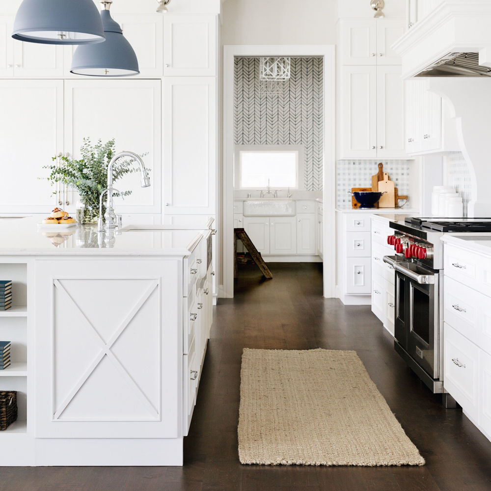 a farmhouse style kitchen with white upper and lower cabinets, white quartz countertops, a large farmhouse sink, and blue pendant lights for a pop of color.