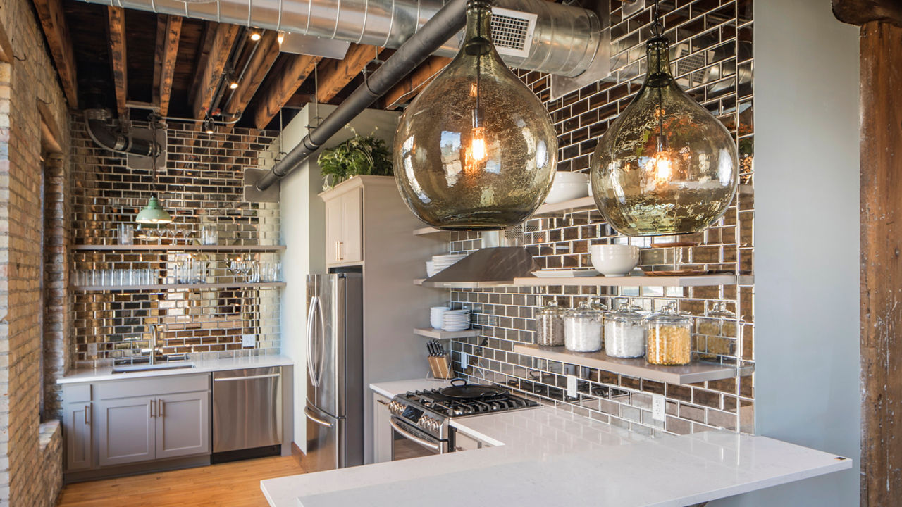 A glam kitchen with white quartz countertops, white cabinets, exposed brick walls, open shelving, and industrial finishes.