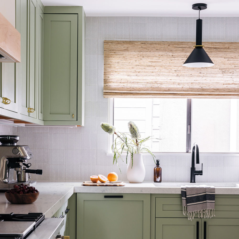 A gorgeous light green kitchen with sage cabinets, white quartz countertops, white tiled backsplash, and modern appliances.