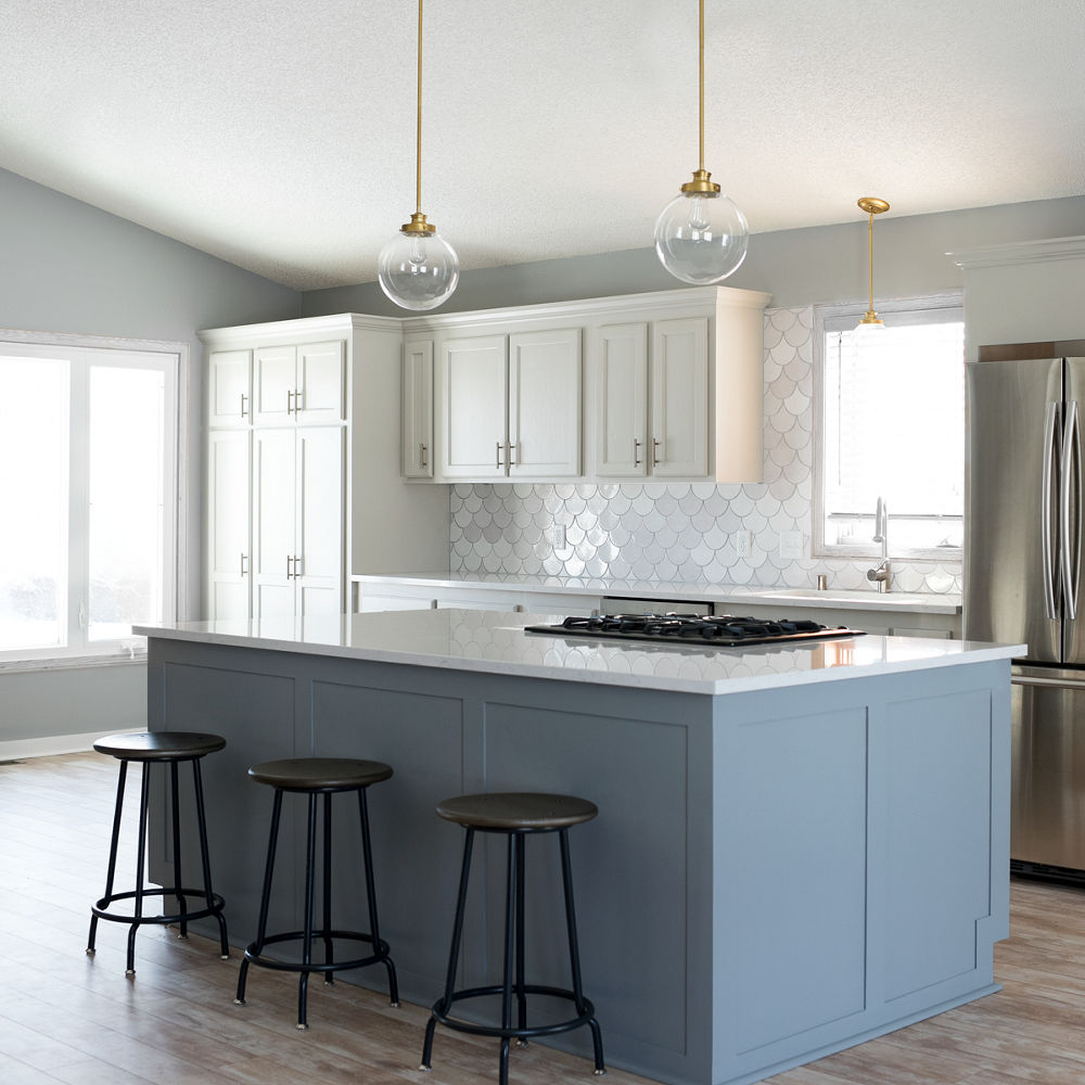 a traditional kitchen white a baby blue island topped with white quartz countertops, three black barstools and pendant lighting