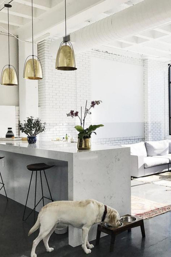 a dog eating out of a free stand dog bowl in a gorgeous kitchen featuring a quartz waterfall island