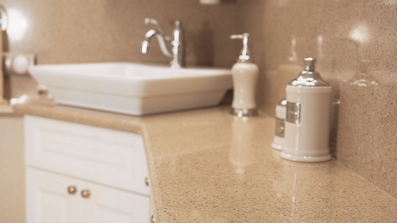 A neutral bathroom with white lower cabinets, brown quartz countertops and matching backsplash, with gold and silver accented nobs and decorations