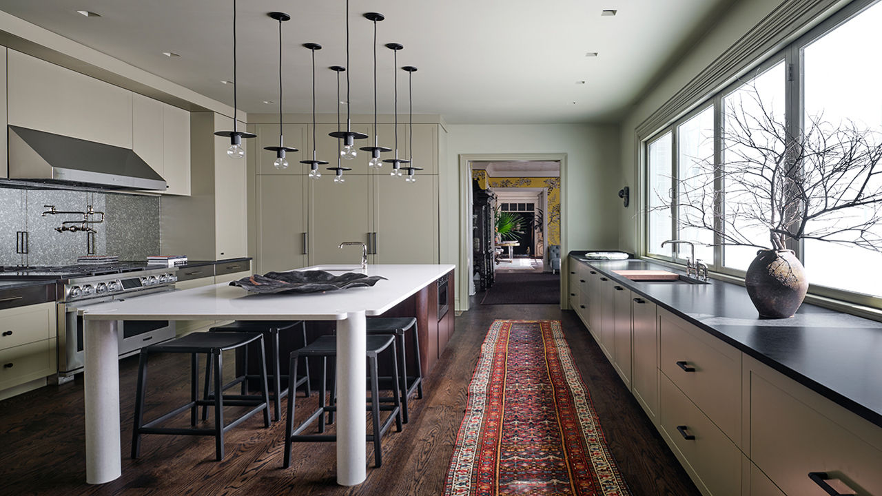 An industrial style kitchen with a large range and hood, black quartz countertops, and a center island with several barstools around it.