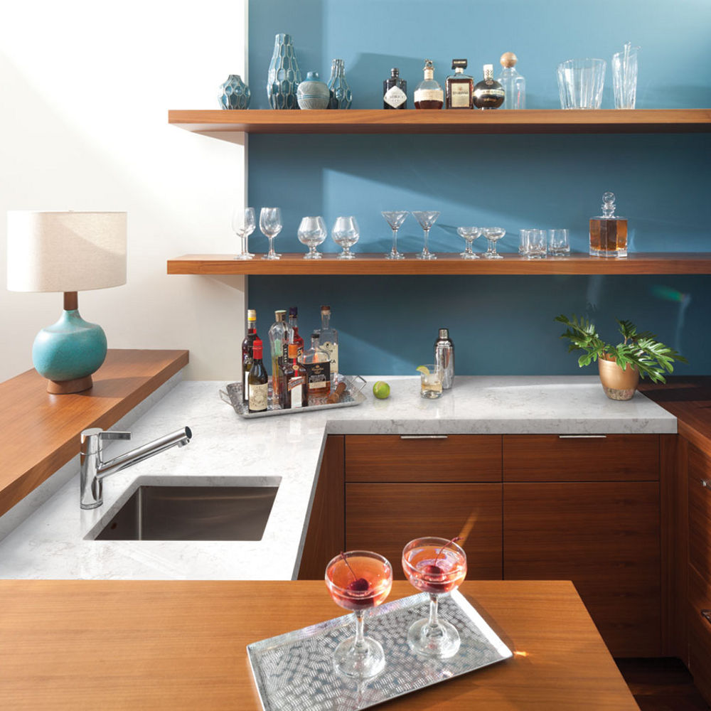 A galley kitchen with wooden cabinets, white quartz countertops, blue painted walls, and open wooden shelving.