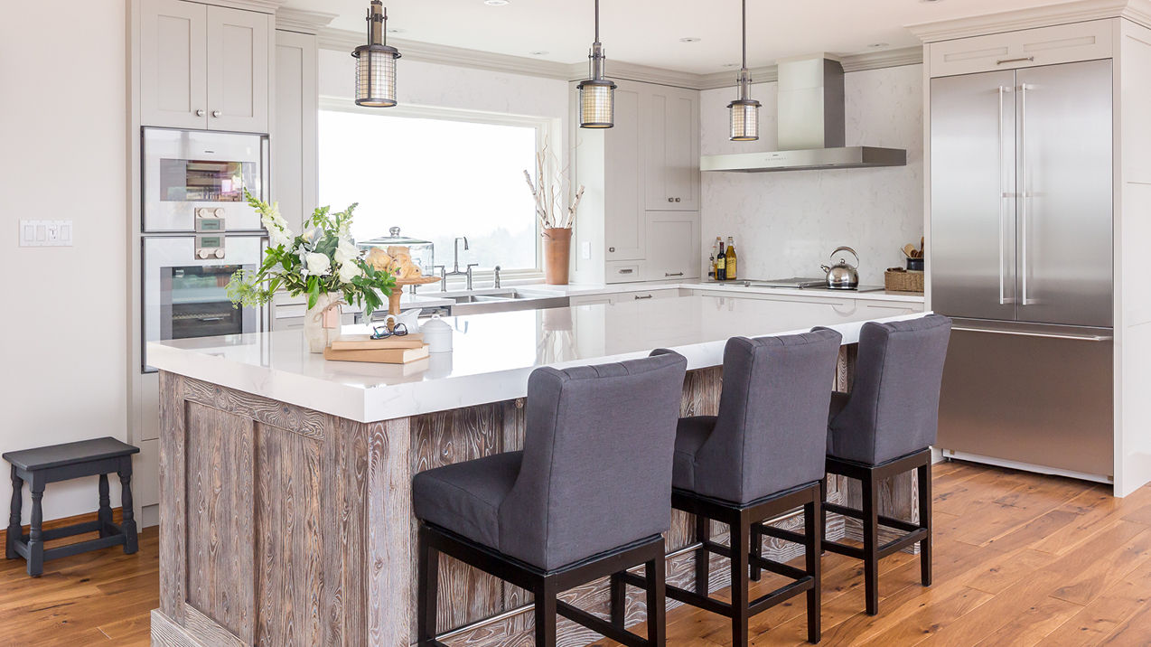 A gorgeous kitchen with a wooden island topped with Cambria Quartz Torquay countertops, three blue barstools, large window over the sink, and modern range.