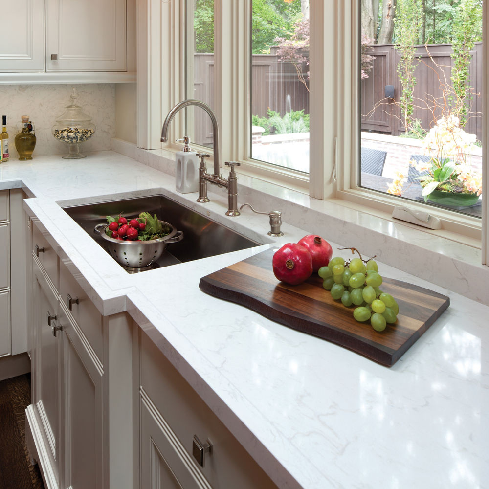 a traditional kitchen with warm gray cabinets, white quartz countertops, and a large sink with fruit in it.