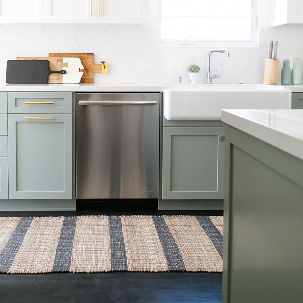 a kitchen with dark wooden floors, light green cabinets, farmhouse sink, white upper cabinets, white quartz countertops, and a small window over the sink.