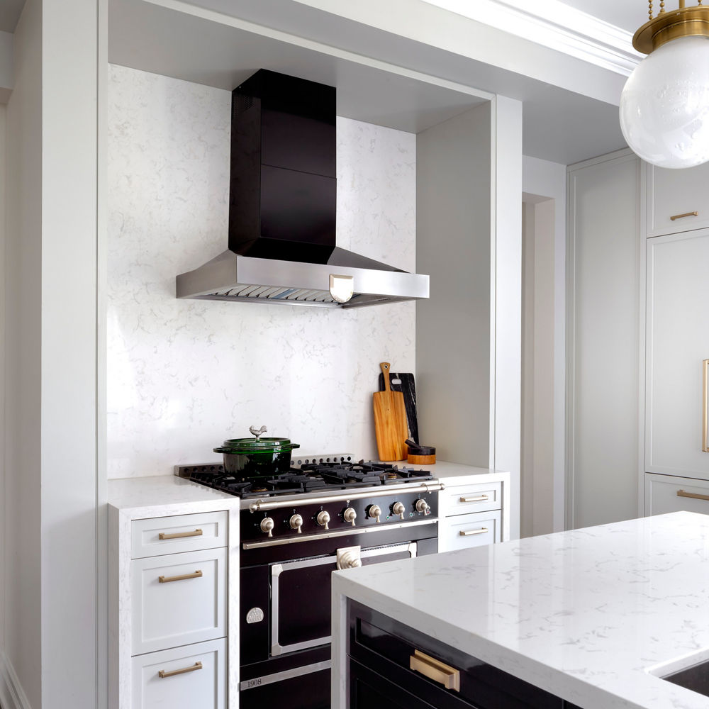 A modern black and white kitchen with black cabinets with gold accents, white quartz countertops, black appliances, a black hood over range, and overhead lighting.