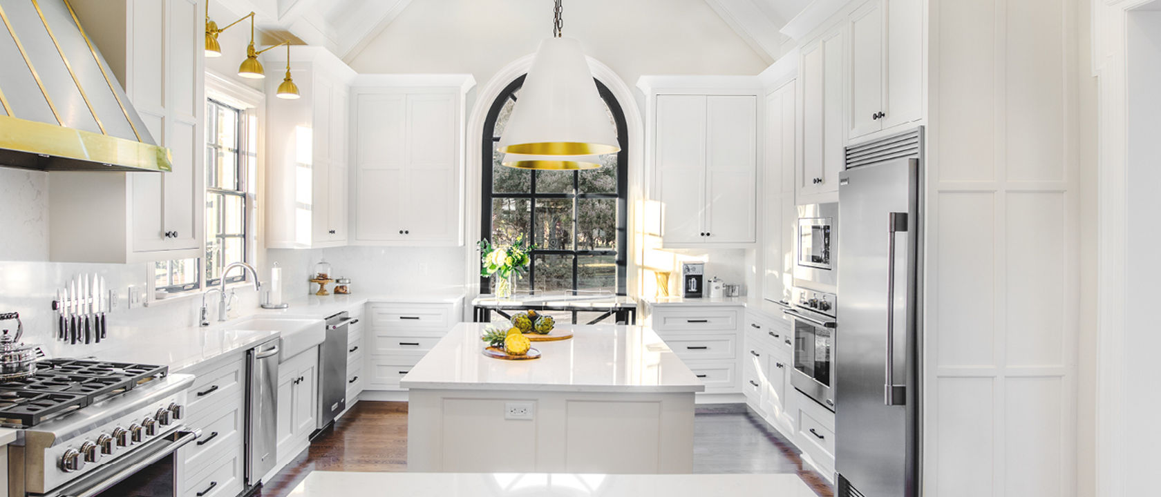 a french countryside inspired kitchen with two islands, white quartz countertops, white cabinets, and gold and black accents throughout.